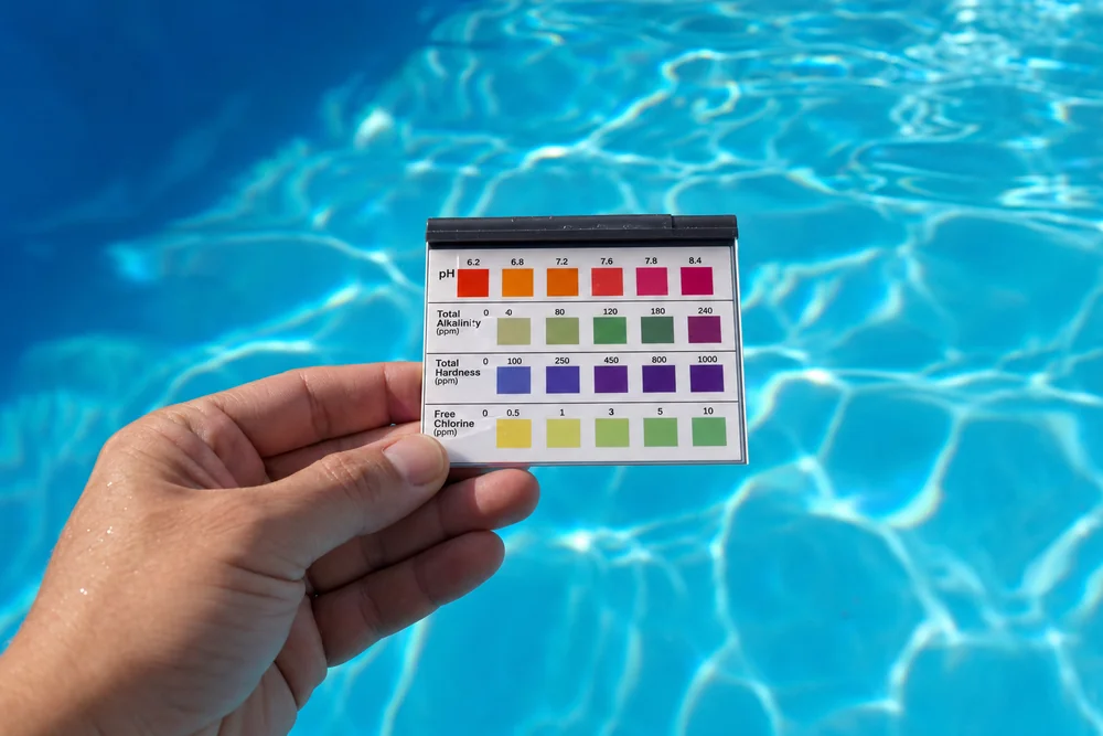 Hand hält Teststreifen mit Chlorwerten vor blaues Poolwasser