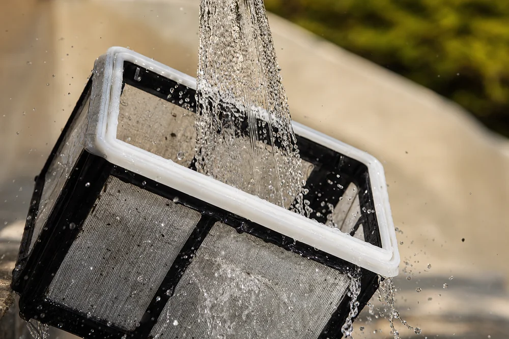 Filterkorb eines Poolroboters wird unter klarem Wasser ausgespült