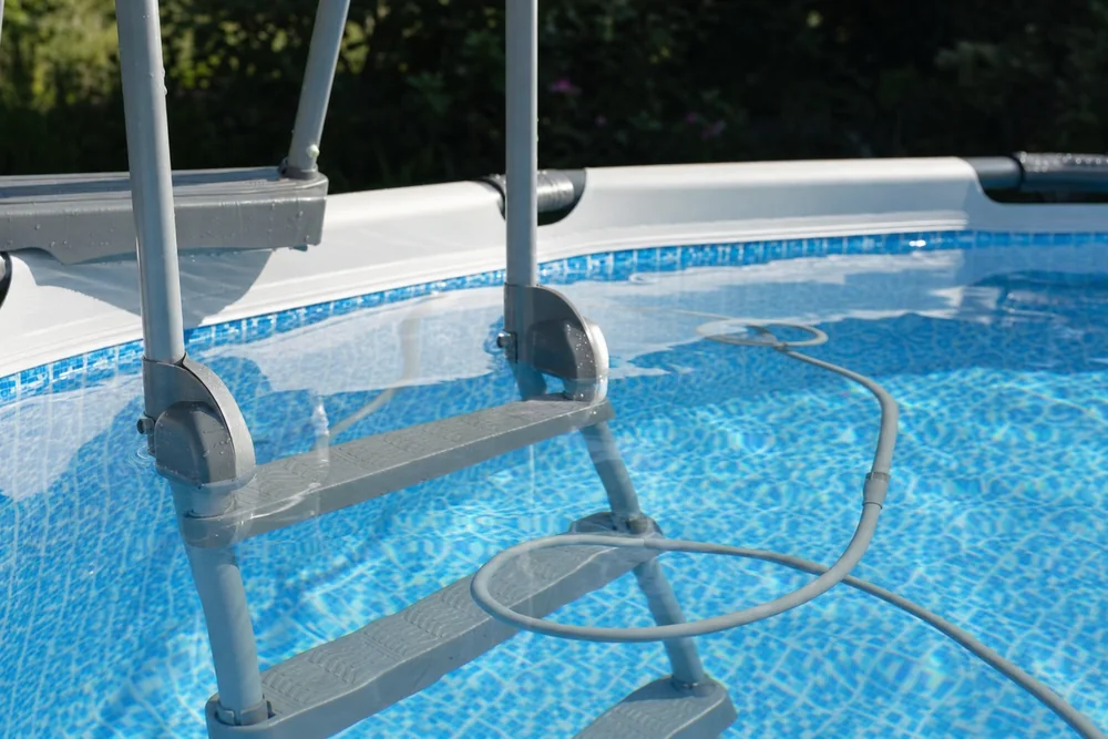 Einstiegsleiter im Aufstellpool neben dem Kabel eines Poolroboters