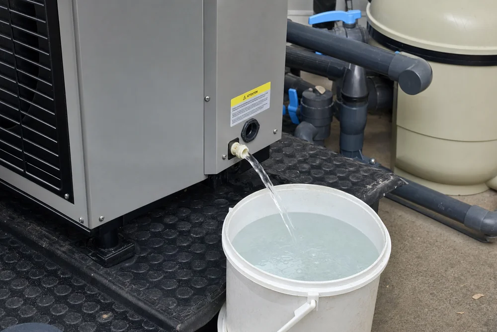 Wasser läuft aus dem geöffneten Ablass einer Pool-Wärmepumpe