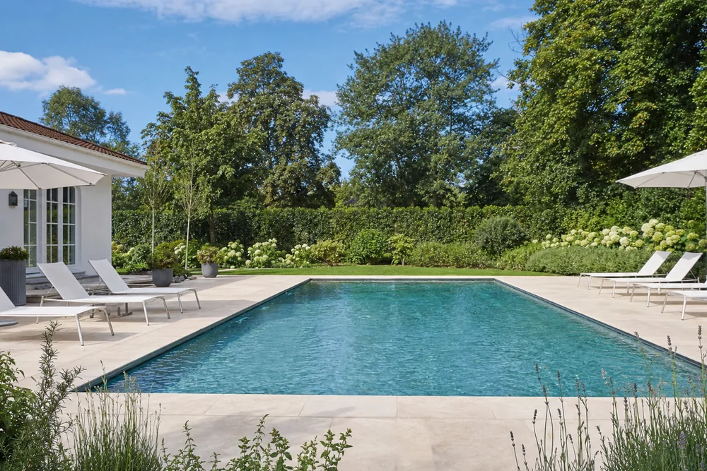 Blick über einen rechteckigen Gartenpool mit umlaufender Terrasse
