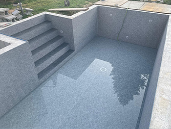 Betonpool im Garten mit hellgrauer, marmorierter Poolfolie, breiter Außentreppe an der Stirnseite.