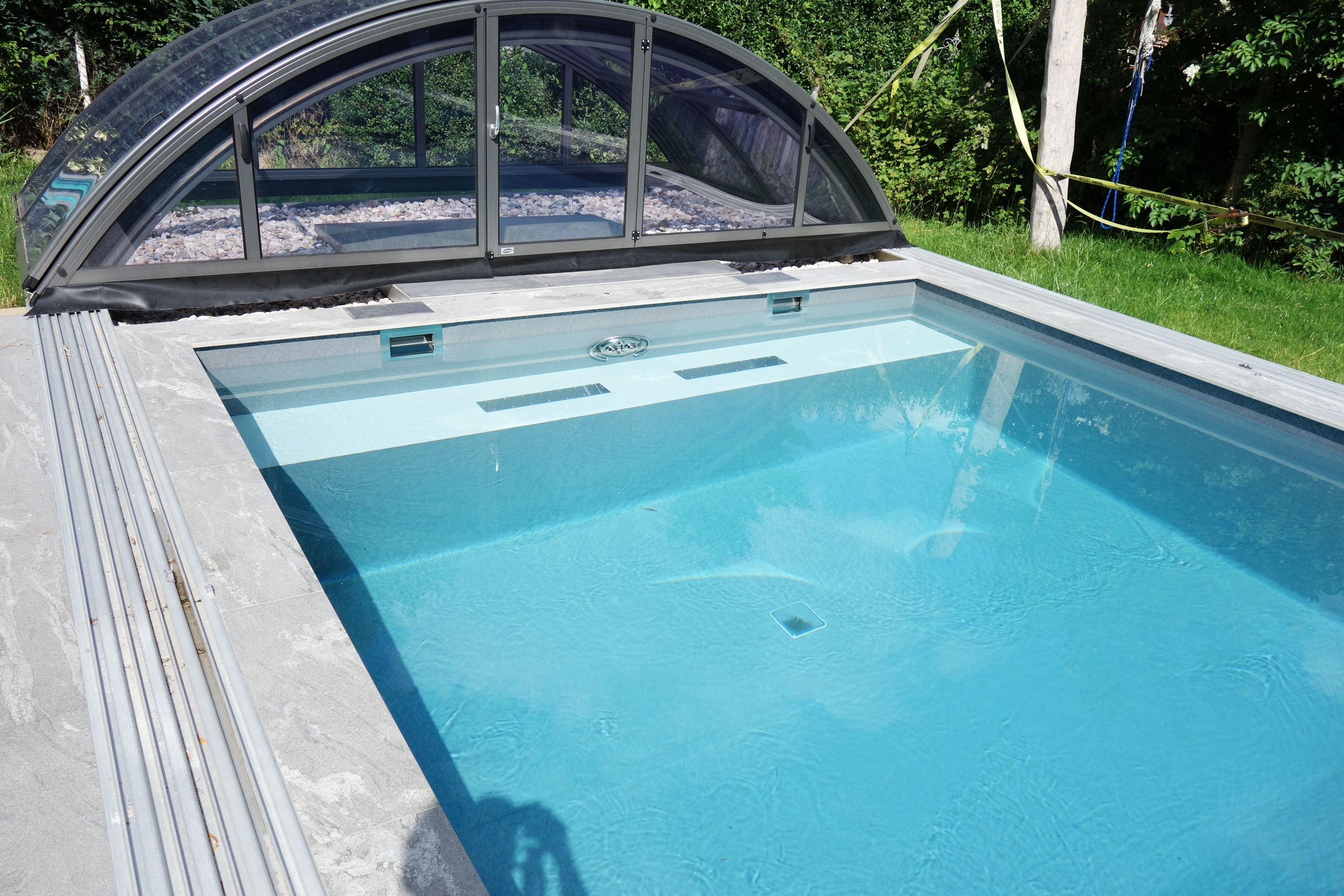 Blick auf das Schwimmbecken mit blauer Folie, Überdachung und grauen Poolrandplatten
