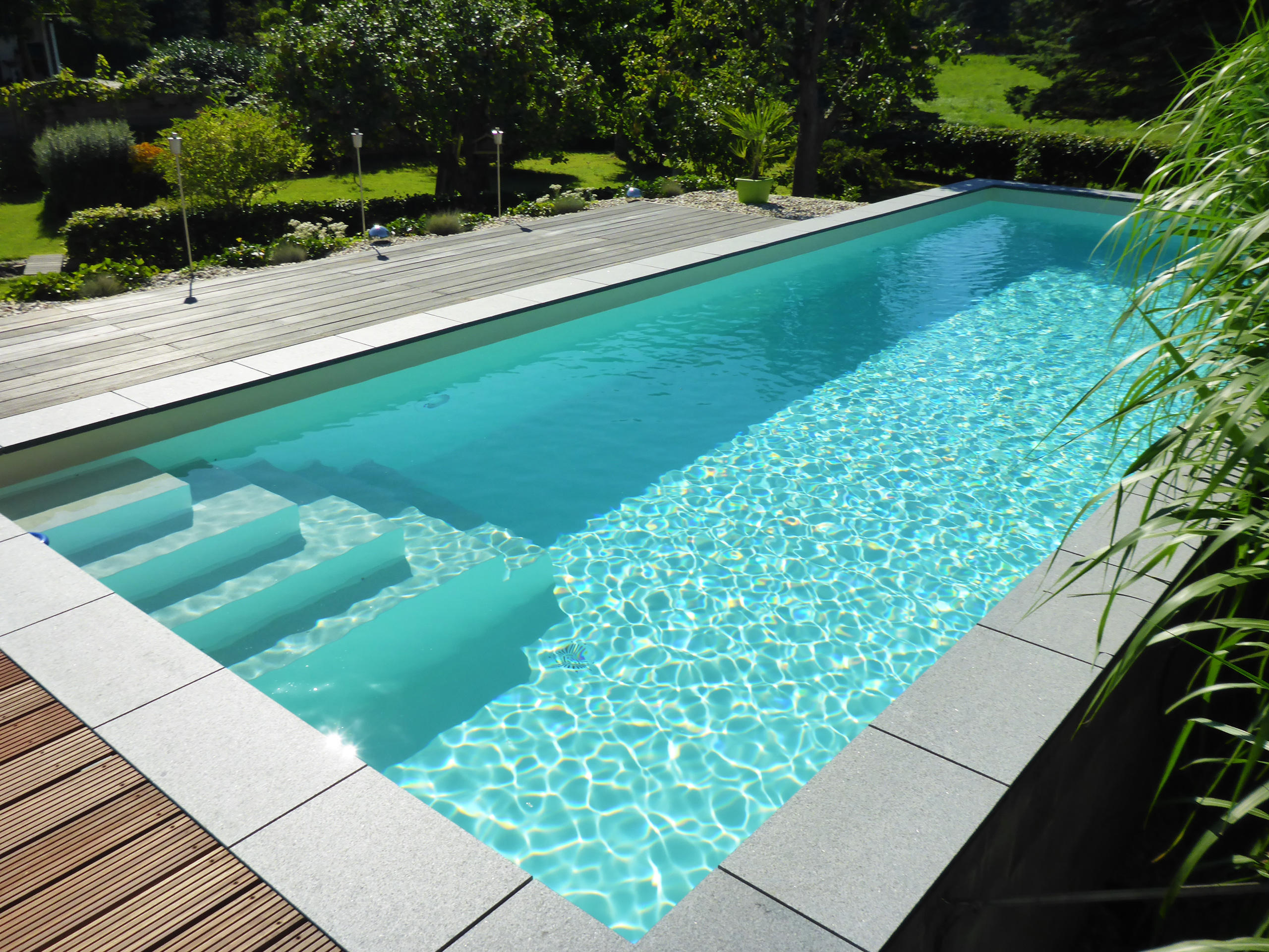 Blick auf den herausstehenden Swimmingpool mit Ecktreppe und Holzterrasse im Garten
