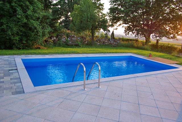 Rechteckbecken mit blauer Einhängefolie, umgeben von hellen Fliesen und einer Edelstahlleiter