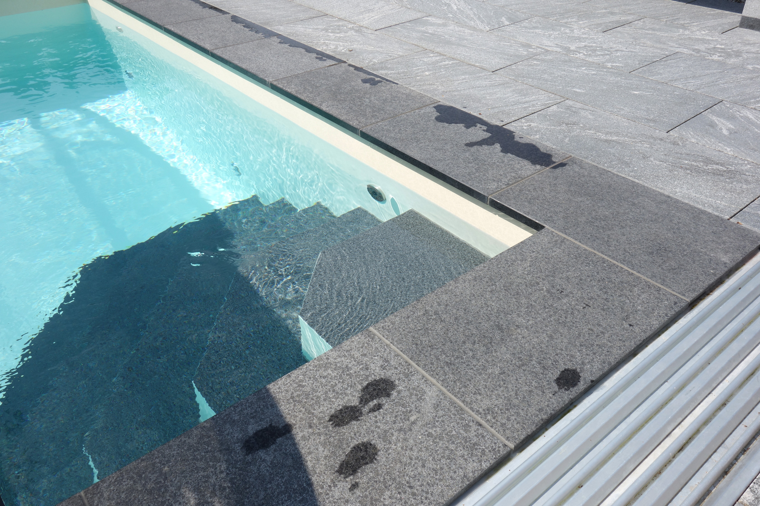Detailansicht der Ecktreppe eines Außenbeckens mit Überdachung und grauen Steinplatten