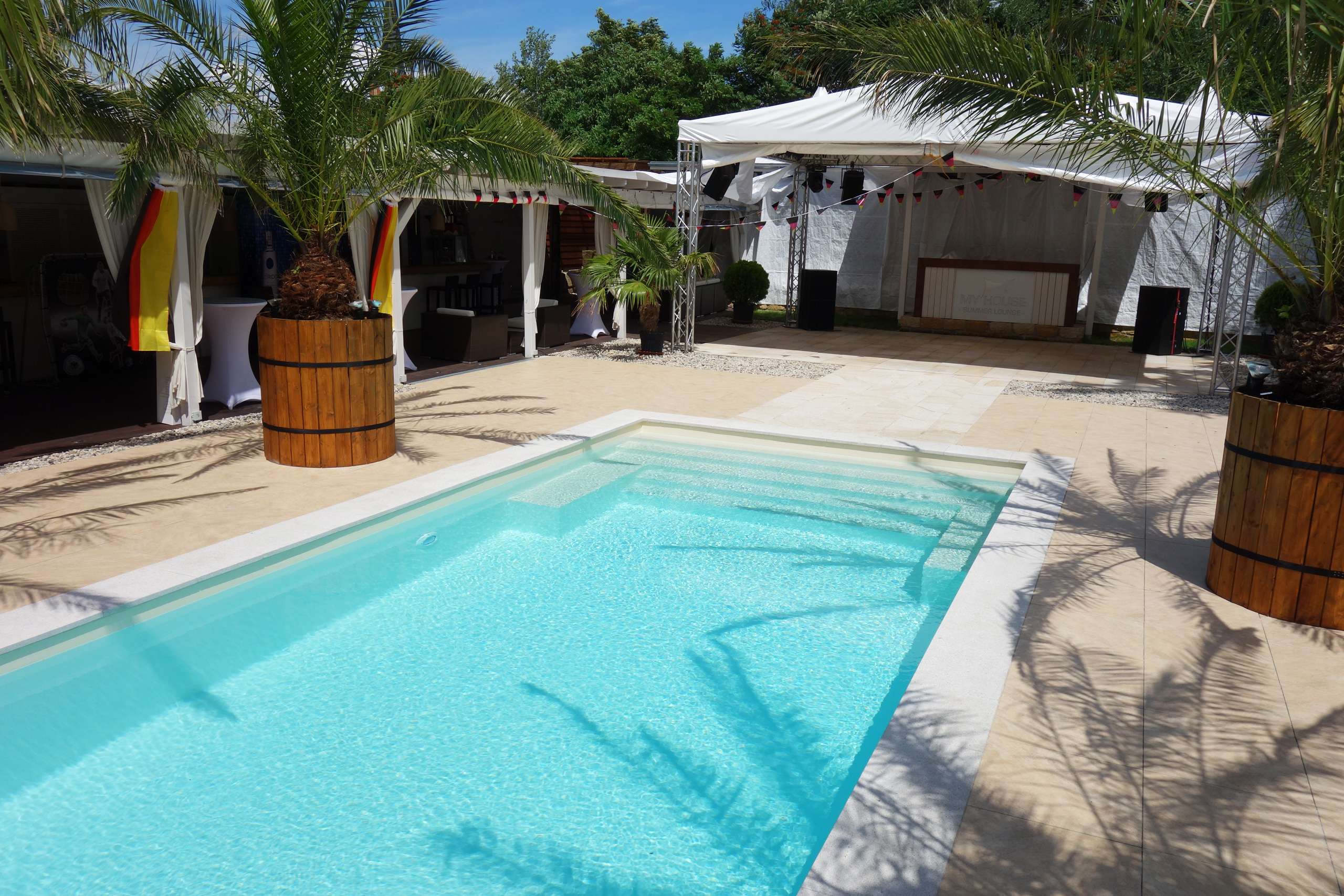 Schwimmbad mit gerader Treppe und Podest, umgeben von Palmen und Partyzelten