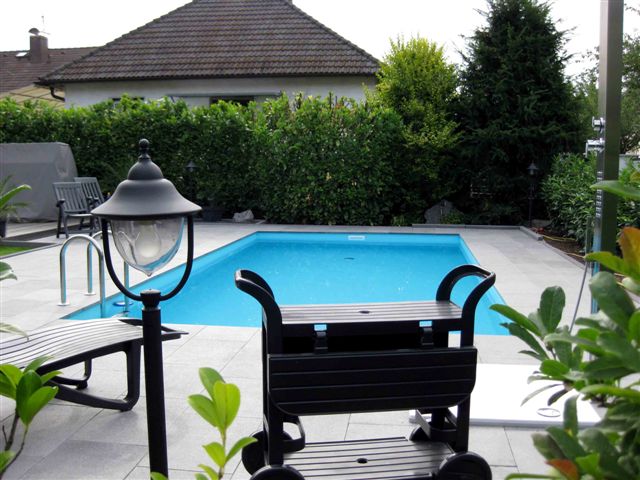 Türkises Schwimmbecken im Garten mit umlaufenden Fliesen und Gartenlaterne im Vordergrund