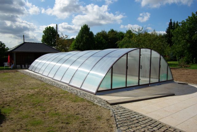 Schwimmbecken 10x4x1,5m mit Treppe und Podest unter transparenter, bogenförmiger Poolüberdachung im Garten