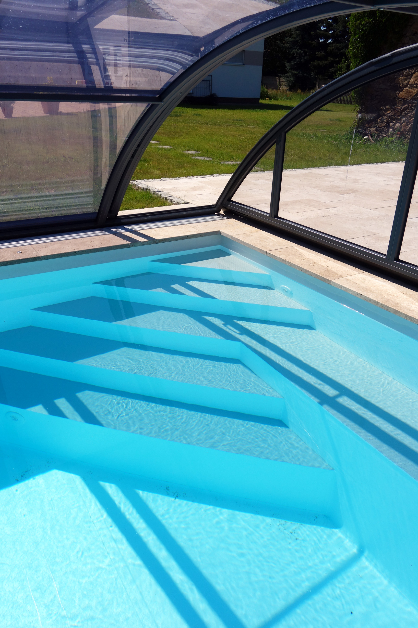 Einstiegstreppe eines Schwimmbeckens mit blauer Folie und Überdachung, von oben fotografiert