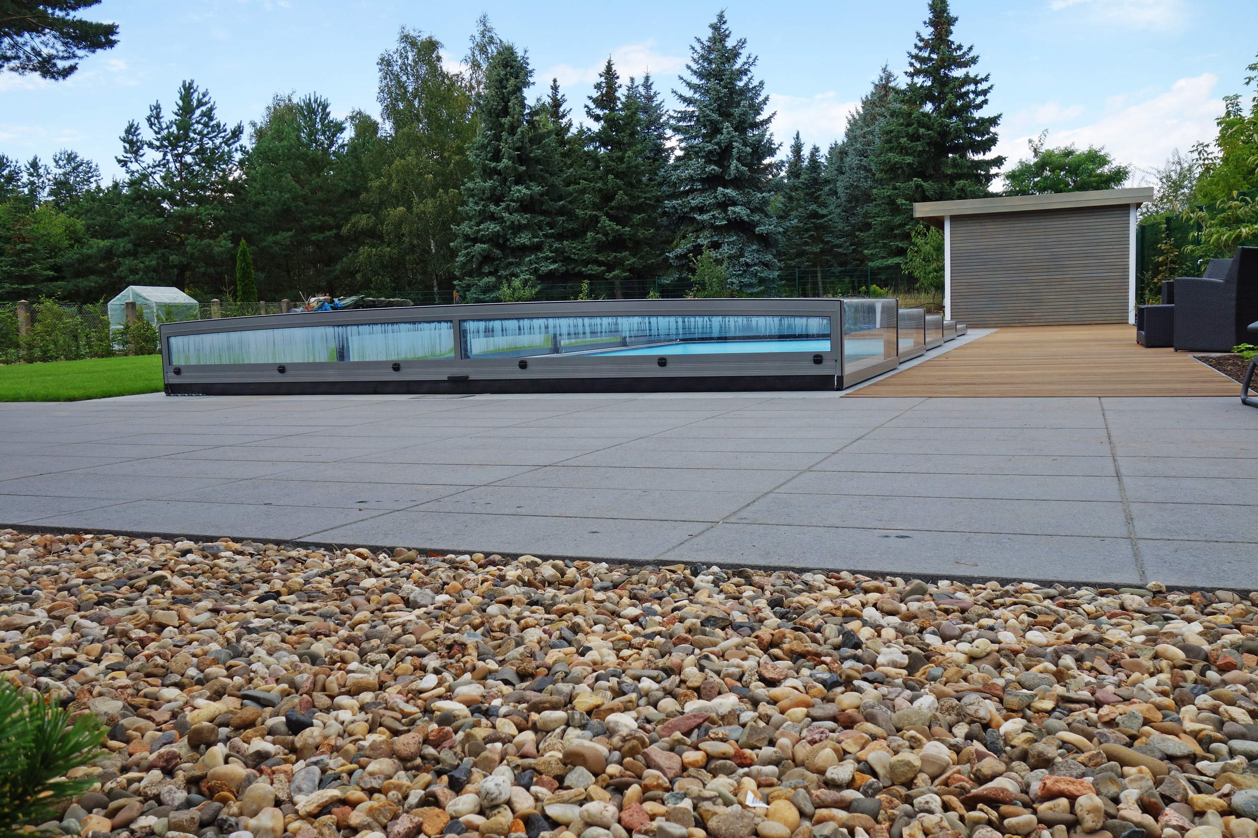 Außenpool 4x10x1,5m mit Überdachung Horizont, umgeben von Kies und einer Holzterrasse
