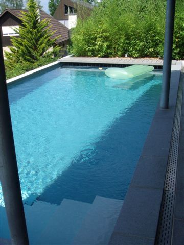 Schwimmbecken mit Granit-Randsteinen, integrierter Treppe und hellblauer Folie, umgeben von Holzterrasse