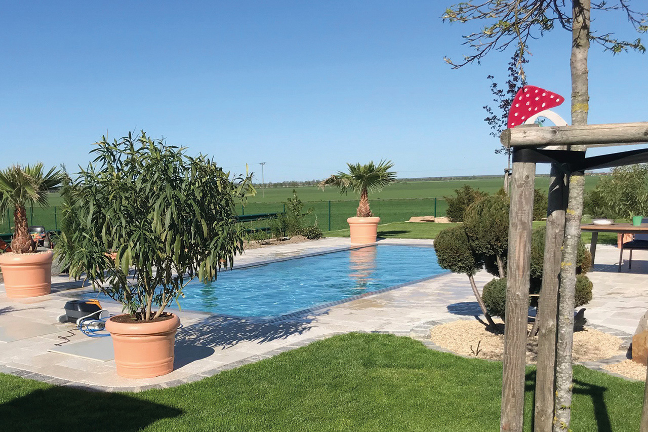 Überlaufbecken Overflow Stone EVO im Garten mit blauer Wasseroberfläche und gepflastertem Randbereich