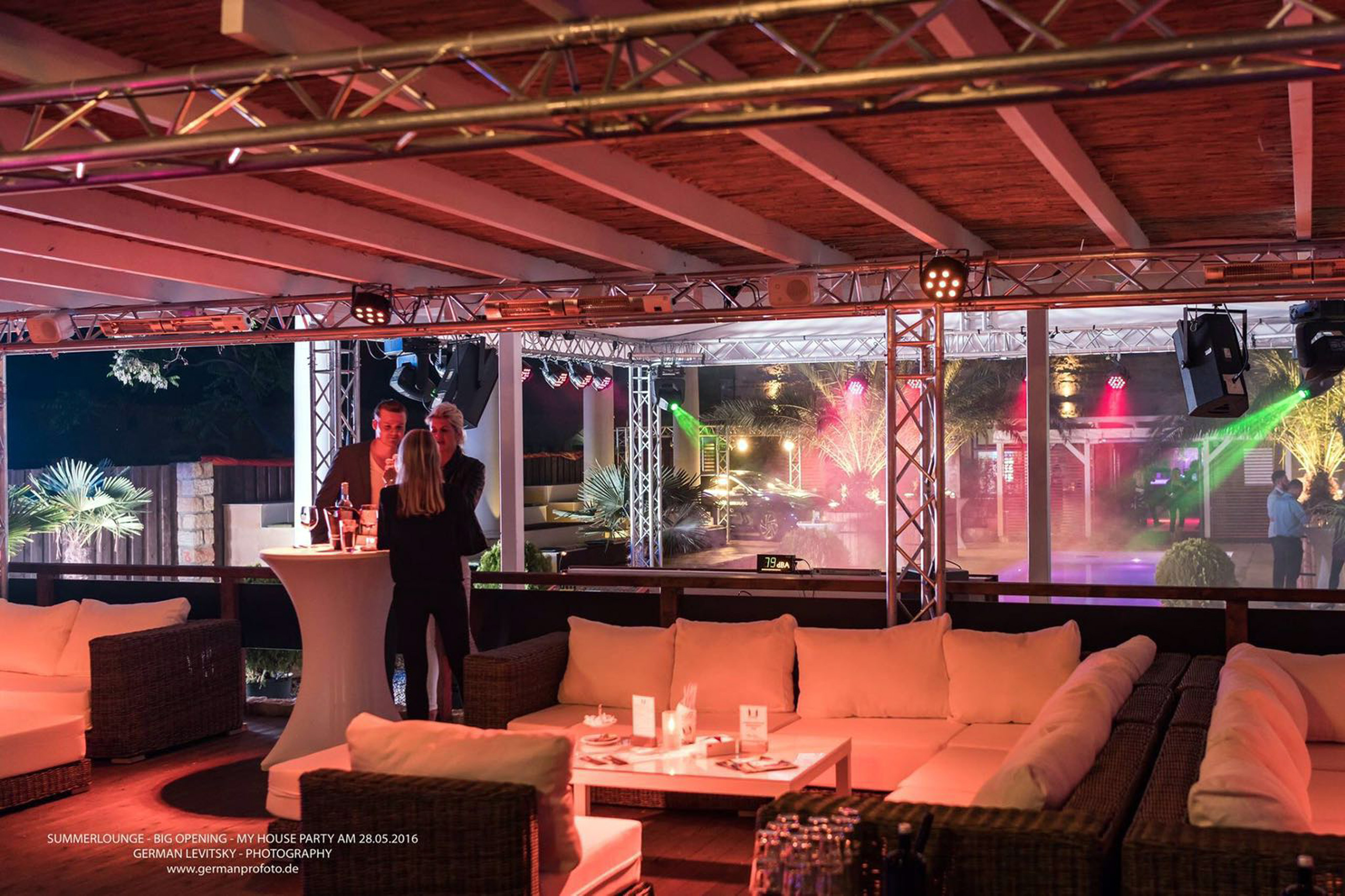 Beleuchtete Lounge-Terrasse mit Partygästen, Heizstrahler und Pool im Hintergrund