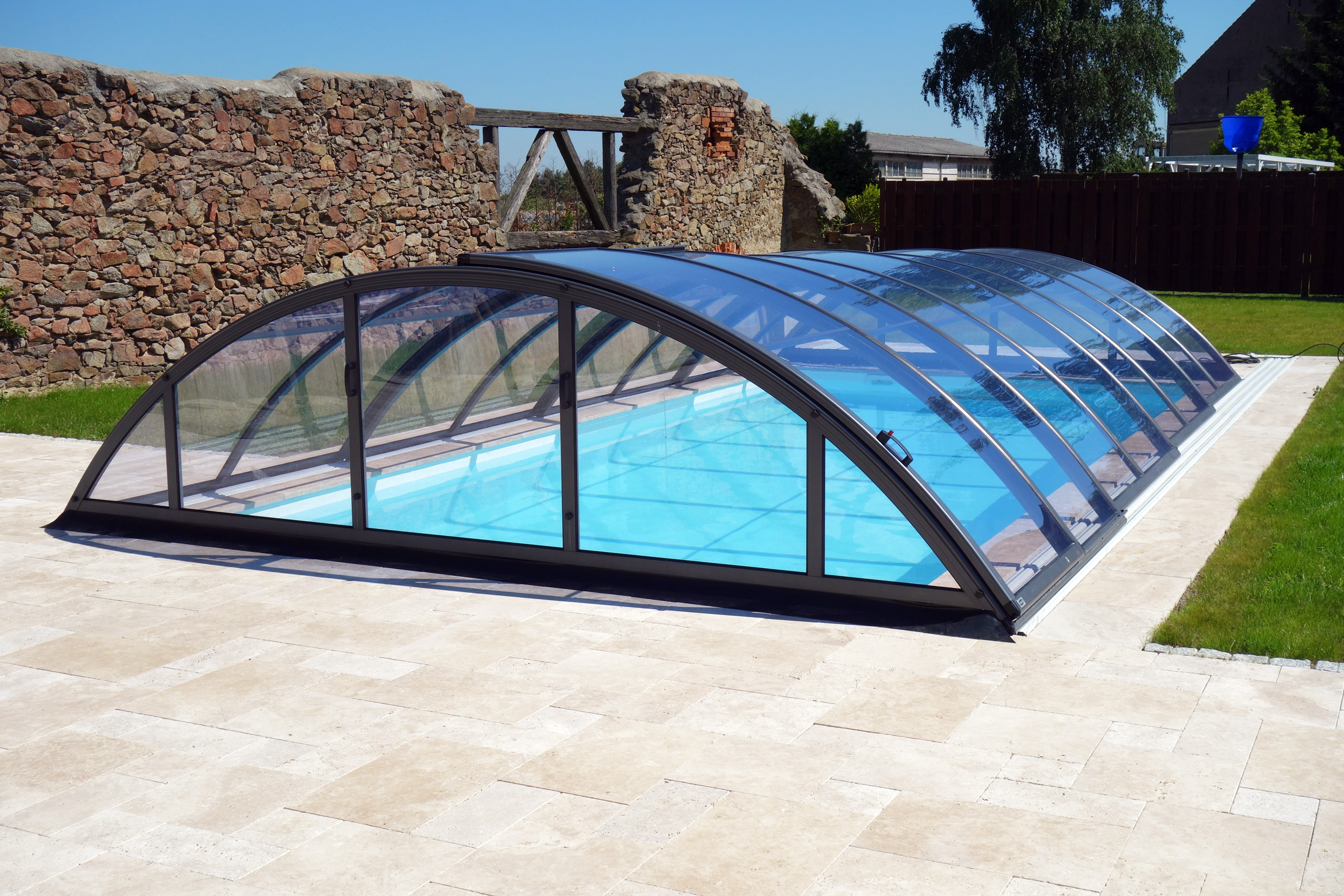 Schwimmbecken mit transparenter, verschiebbarer Überdachung auf beigefarbenen Terrassenplatten