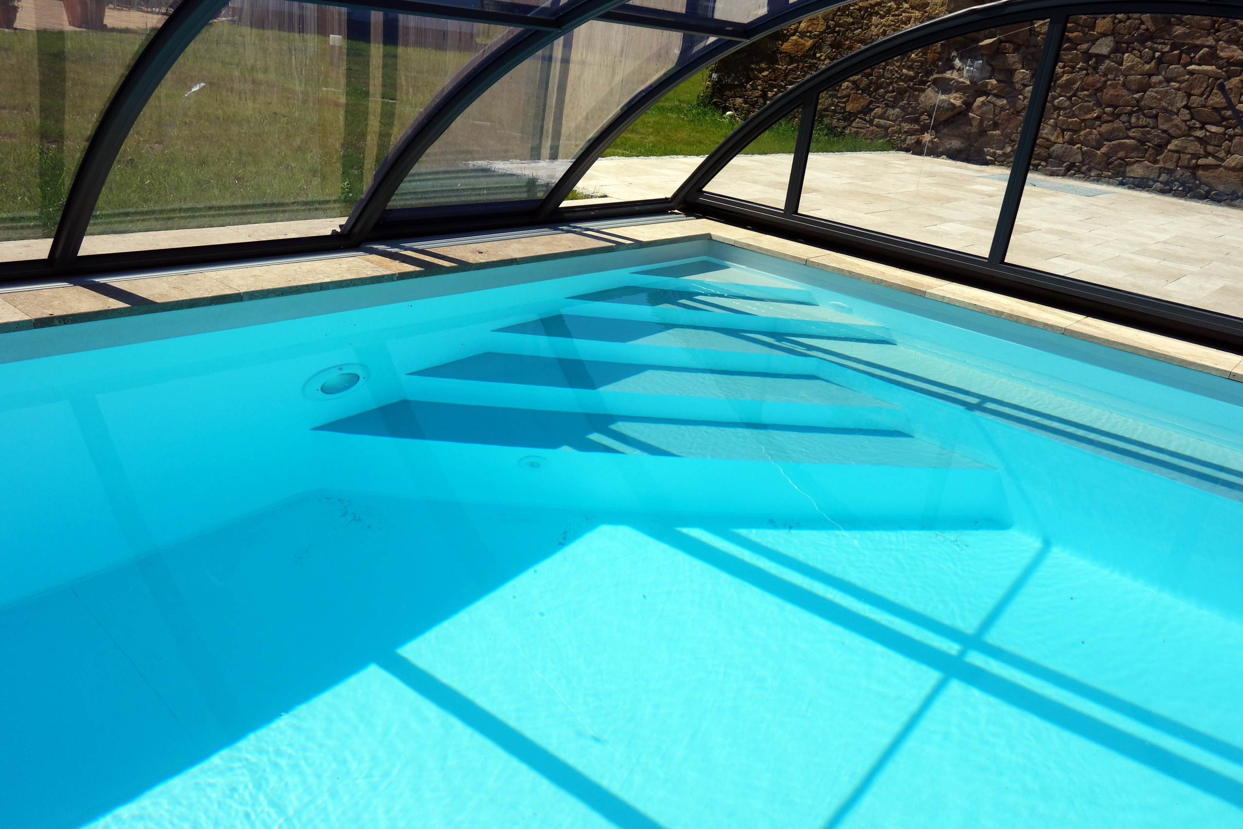 Blick ins Schwimmbecken mit Unterwasserscheinwerfer und breiter Treppe unter der Poolüberdachung