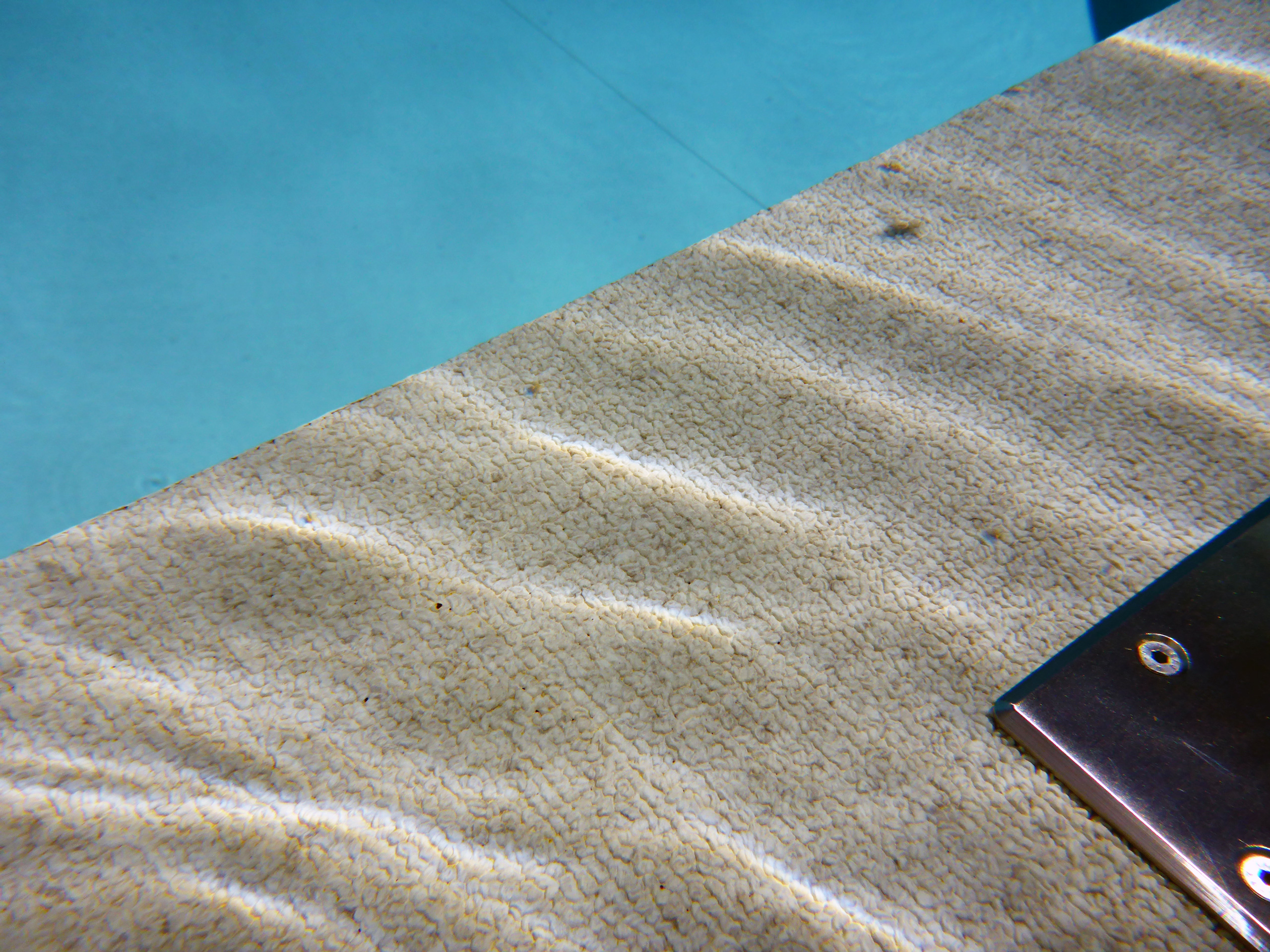 Detailansicht der strukturierten Oberfläche einer Pooltreppe unter Wasser mit blauem Poolwasser
