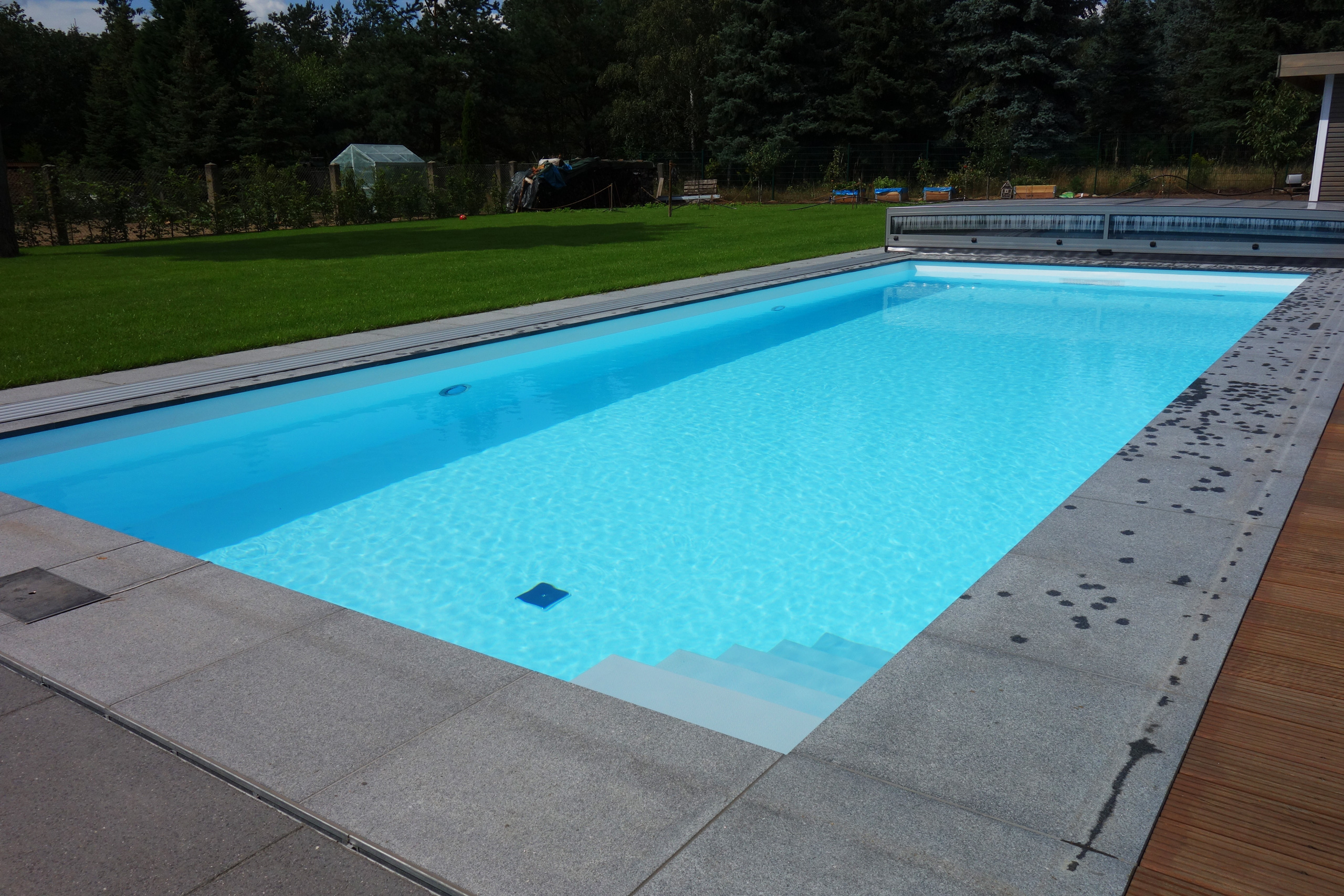 Gerade Treppe im Außenpool mit blauer Folie, umgeben von grauen Fliesen und Holzterrasse