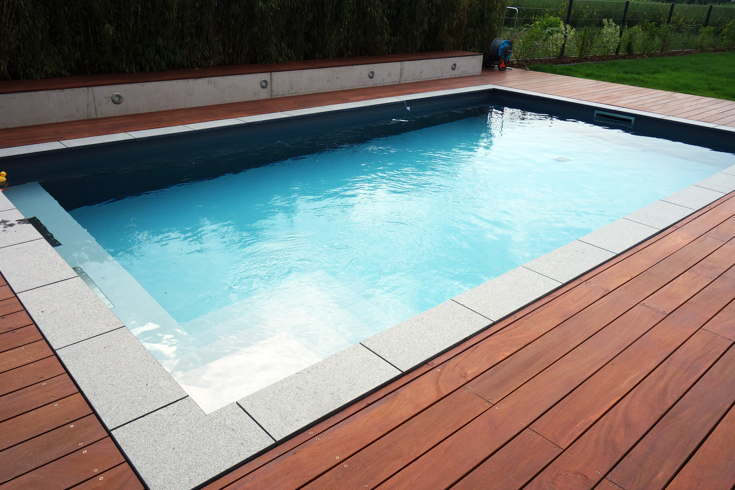 Betonbecken 3,5x7x1,5m mit Ecktreppe und Podest, umgeben von Holzterrasse und Steinplatten