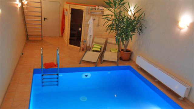 Hallenbecken mit blauer Einhängefolie, Poolleiter, Sauna und Liegestühlen in einem privaten Wellnessbereich.