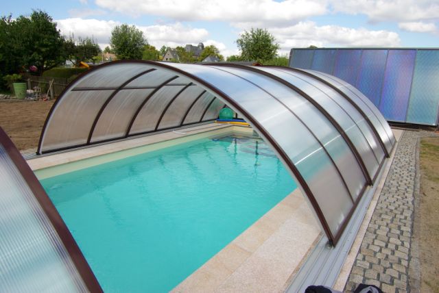 Teilweise geöffnete, transparente Poolüberdachung über einem Schwimmbecken mit hellblauer Folie