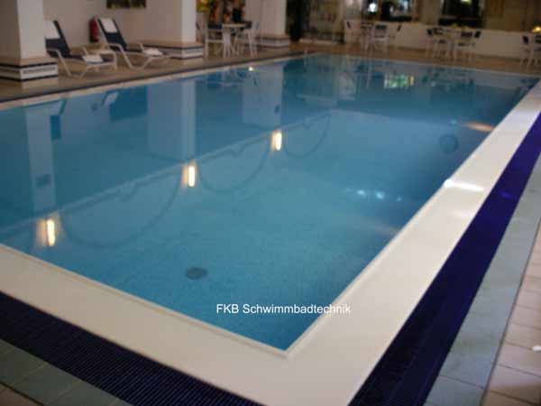 Schwimmbecken mit blauer Folie und weißer Überlaufrinne, umgeben von dunklen Bodenfliesen.