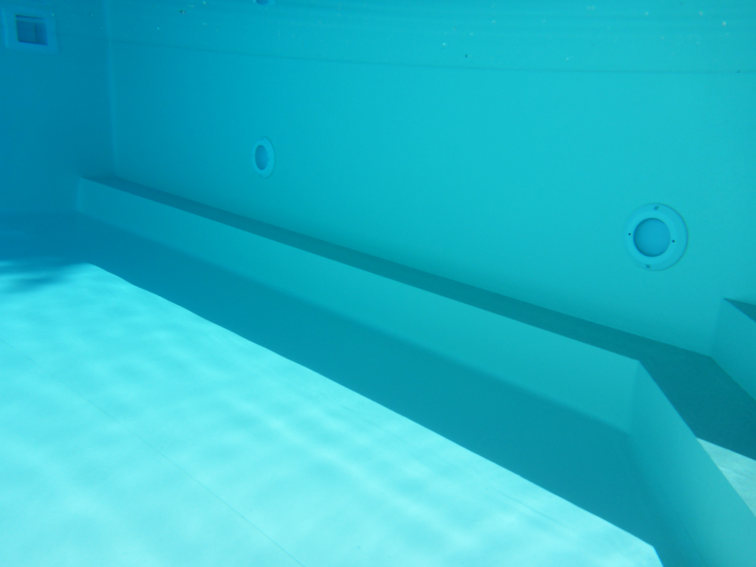 Unterwasseransicht des Rechteckpools mit Stehstufe, Einbauteilen und Lichtreflexionen auf dem Boden.