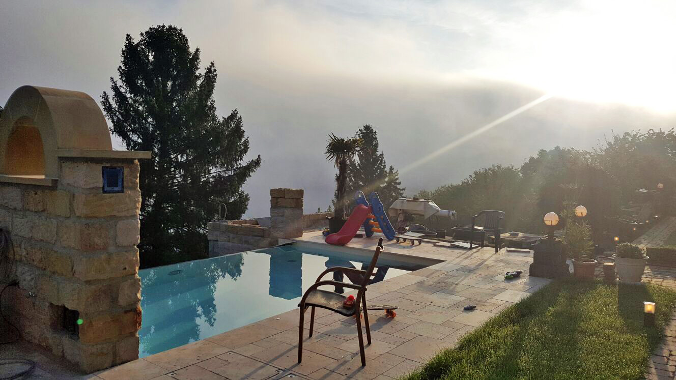 Überlaufbecken Infinity Pool mit Ecktreppe und Sitzbank, umgeben von Terrasse und Garten.