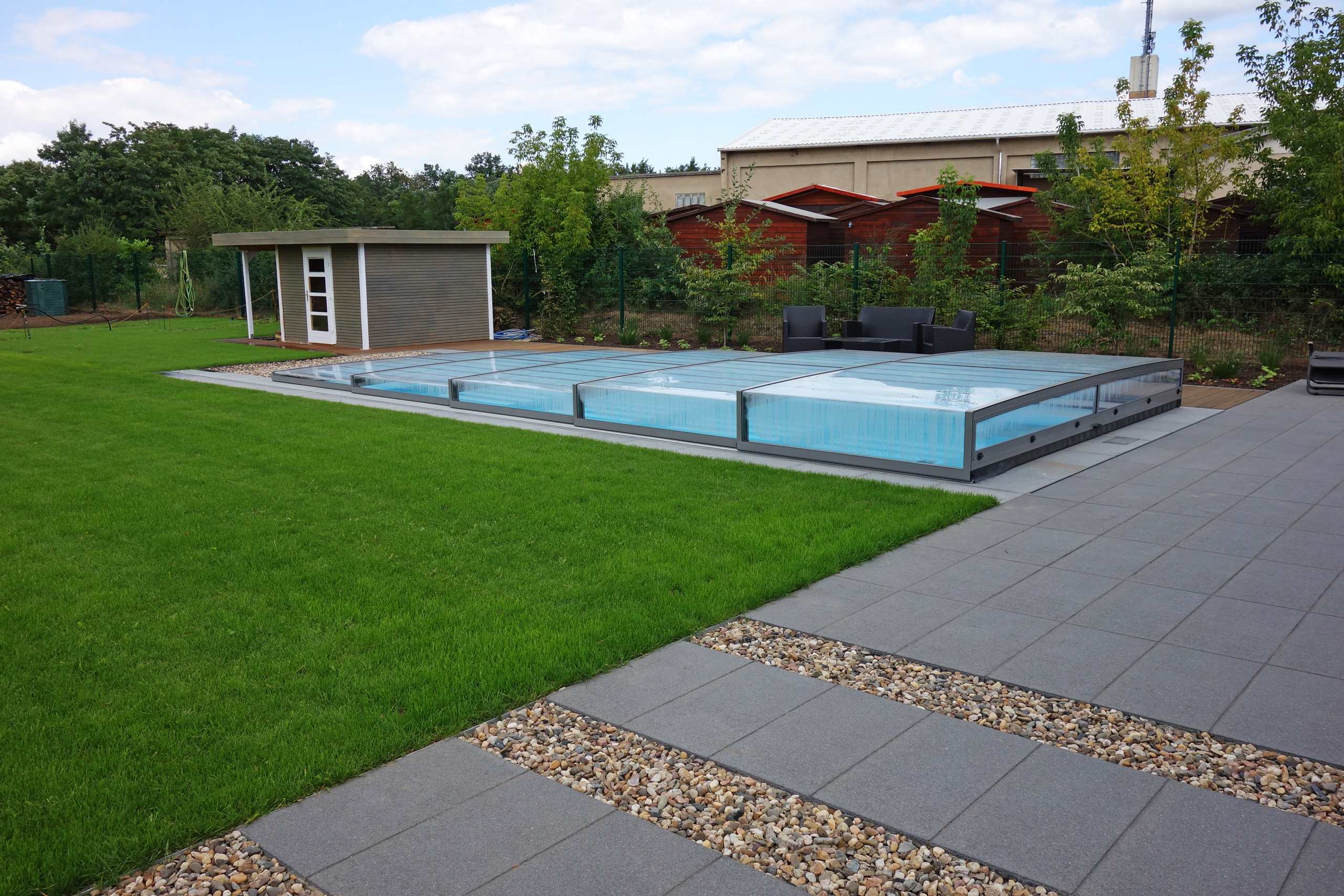 Überdachter Außenpool mit Strömungsturbine, umgeben von Rasen, Terrasse und Gartenhaus