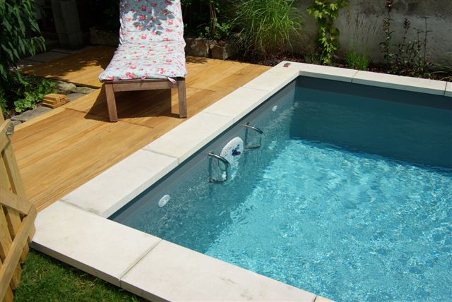 Detailansicht des Schwimmbeckens mit Einstiegsleiter und Holzterrasse, umgeben von Grünflächen.