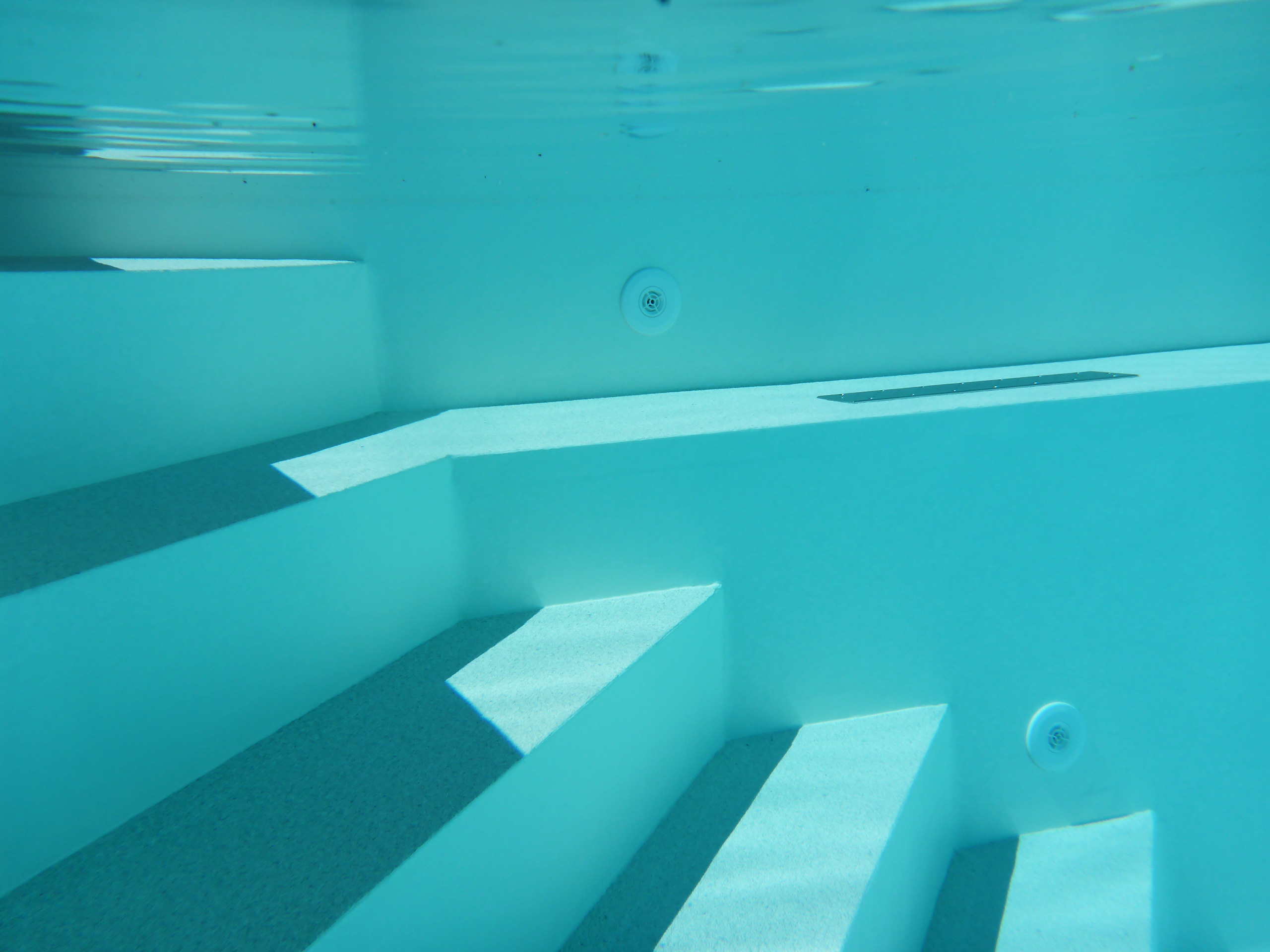 Unterwasseransicht der weißen Ecktreppe mit Stehstufe und Einbauteilen im Pool