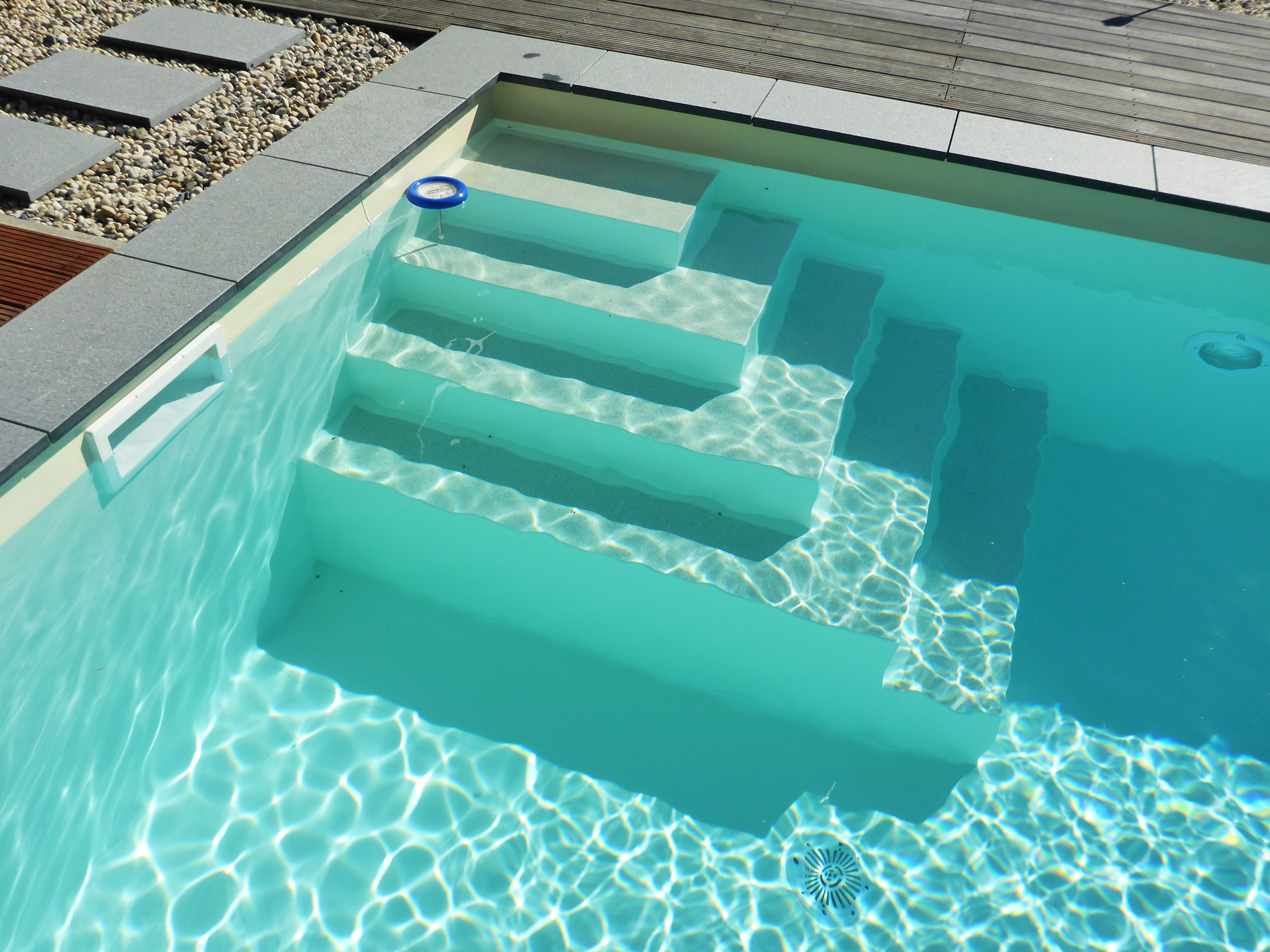 Ecktreppe und Skimmer im Swimmingpool mit blauer Folie, umgeben von grauen Platten und Holzdielen