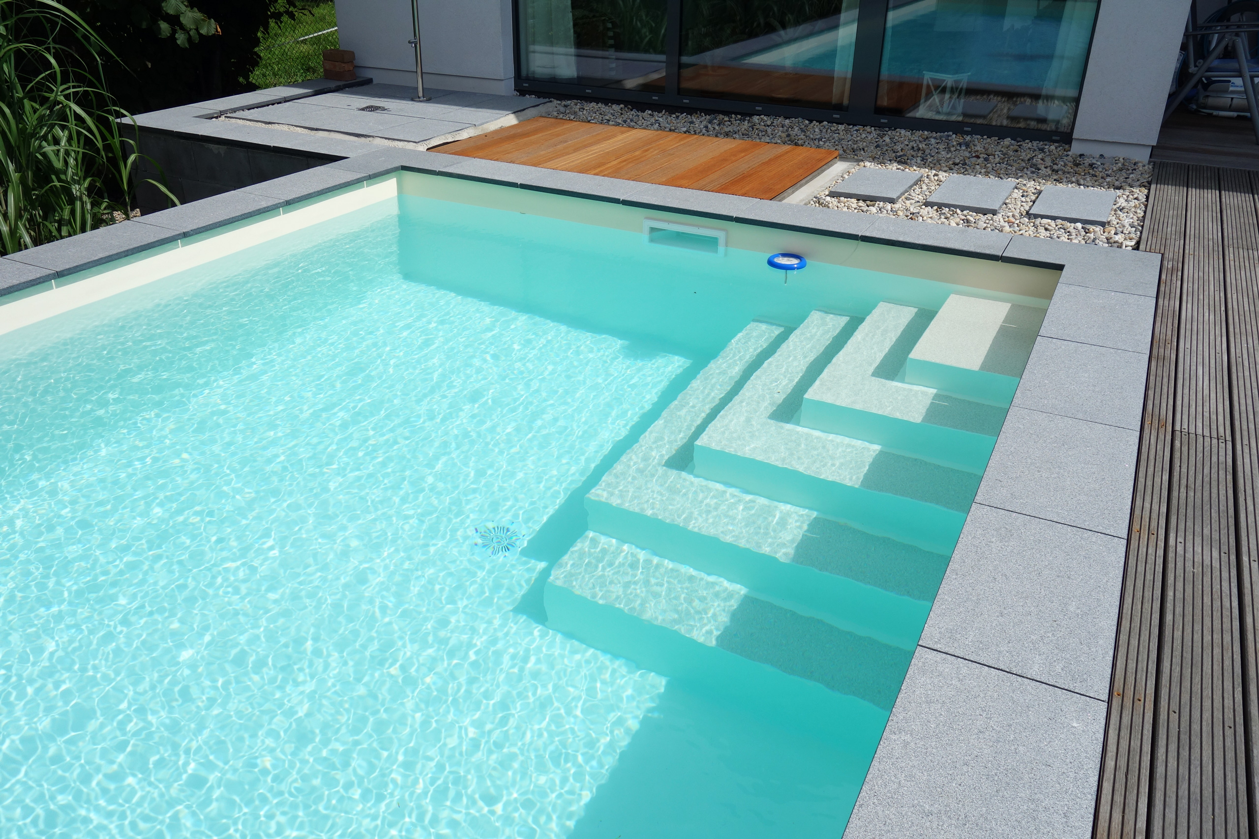 Detailansicht der Ecktreppe eines Swimmingpools mit hellblauer Wasseroberfläche und grauem Randstein
