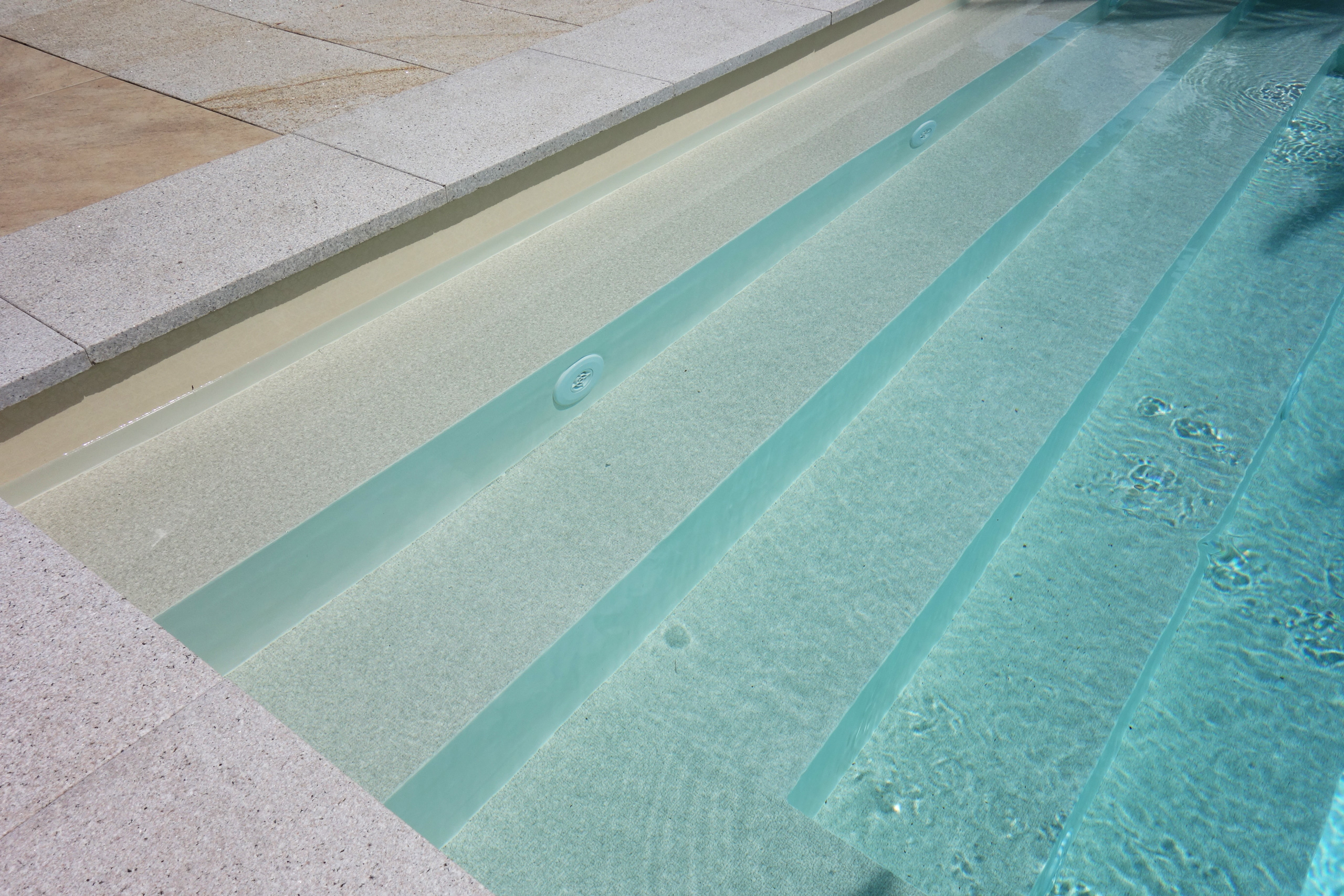 Gerade Treppe und Podest eines Schwimmbads mit sandfarbener Folie und hellen Beckenrandsteinen