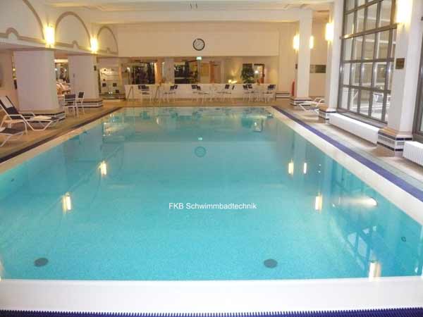 Saniertes Schwimmbecken mit Überlaufrinne und hellblauer Folie in einem Innenbereich mit Liegen und Tischen