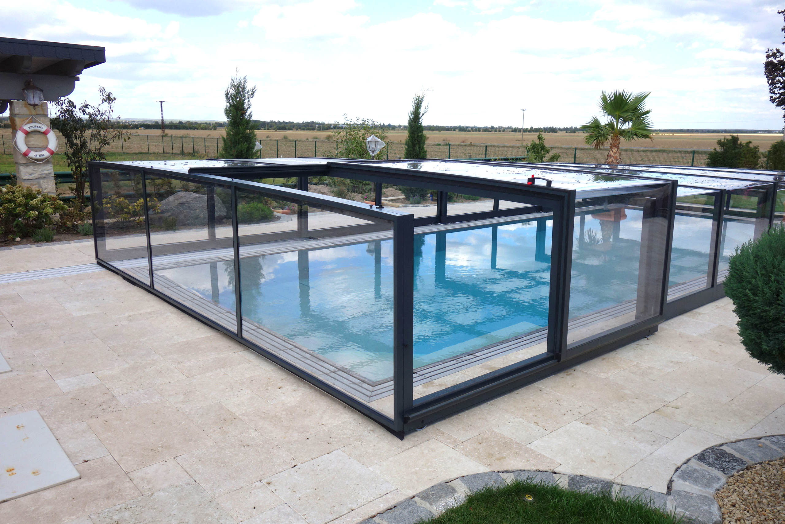Poolüberdachung Prestige Plus mit transparenten Segmenten und schwarzem Rahmen auf hellen Fliesen.
