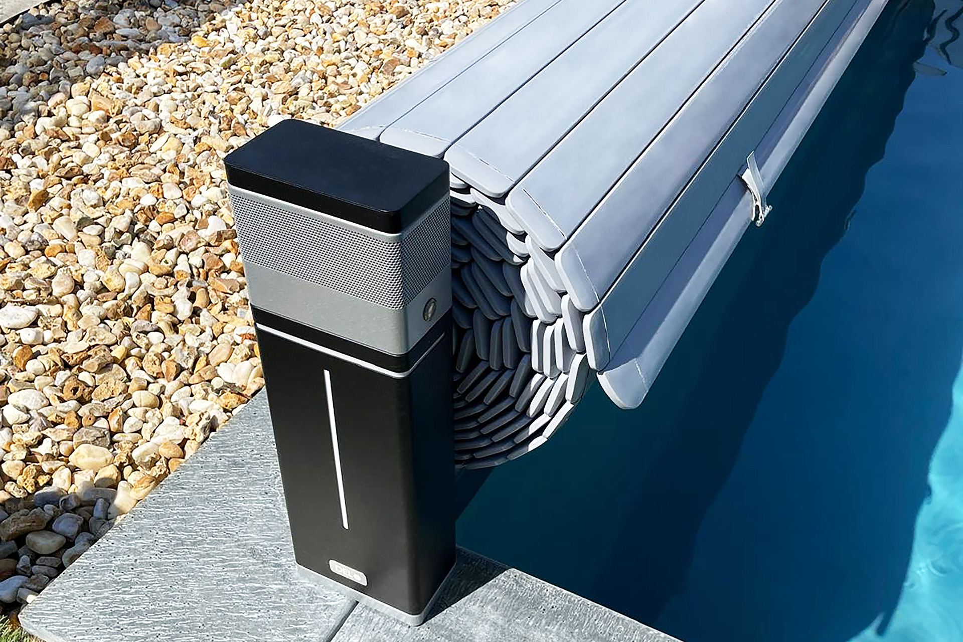 Detailansicht des schwarzen elektrischen Pool Aufrollers Tixit mit aufgerollter Rollladenabdeckung am Beckenrand.