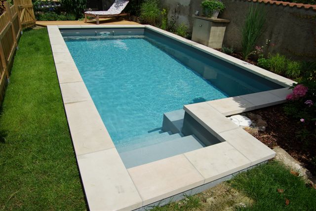 Eingelassenes Schwimmbecken mit Treppe, umgeben von hellem Randstein und Rasen im Garten