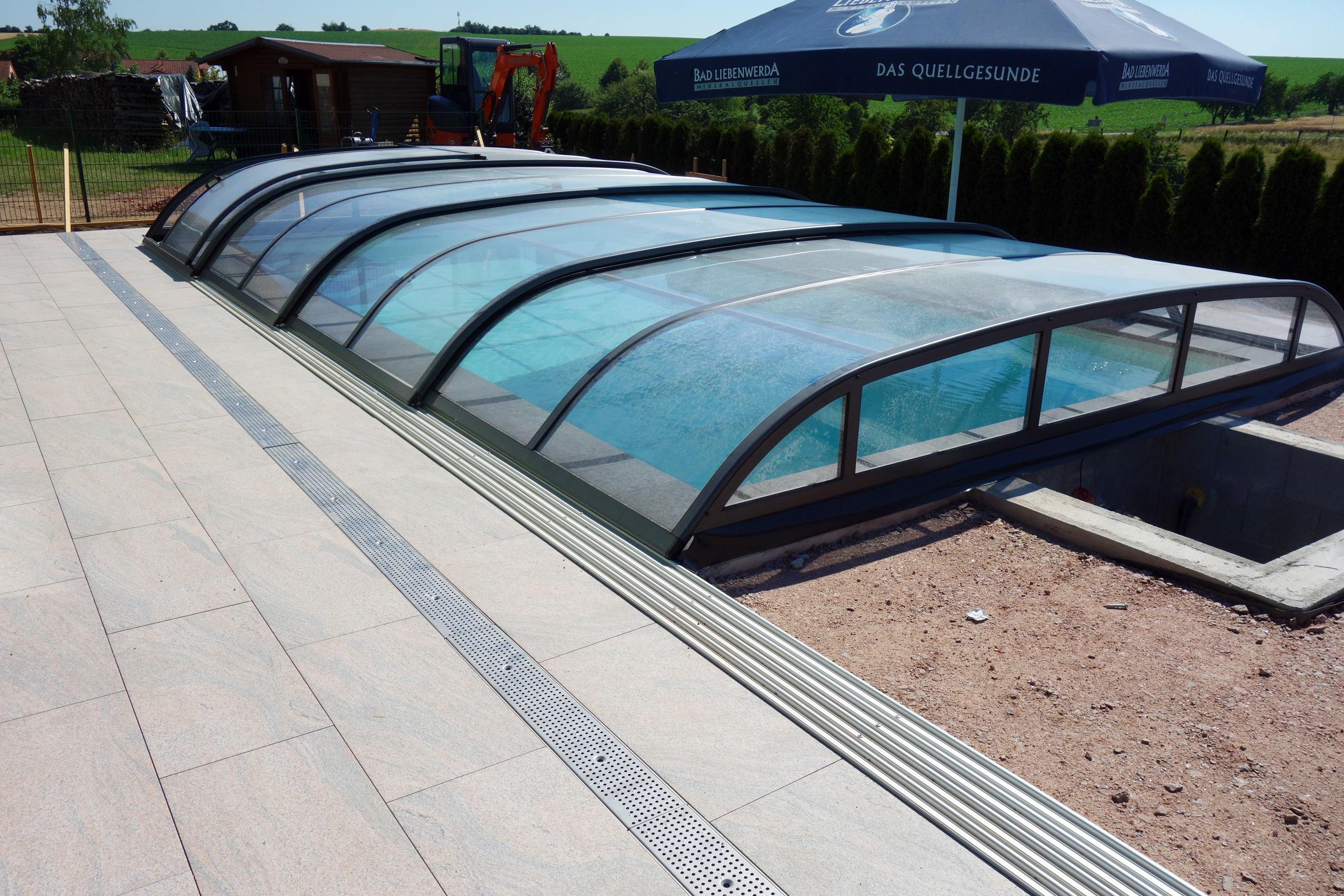 Detailansicht der Poolüberdachung mit Schienen und Entwässerungsrinne auf der Poolumrandung