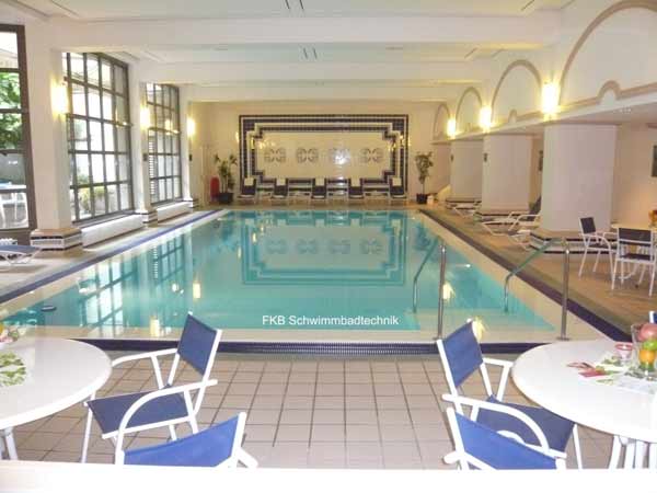 Innenpool mit Überlaufrinne und Sitzgelegenheiten, umgeben von großen Fenstern und Säulen.