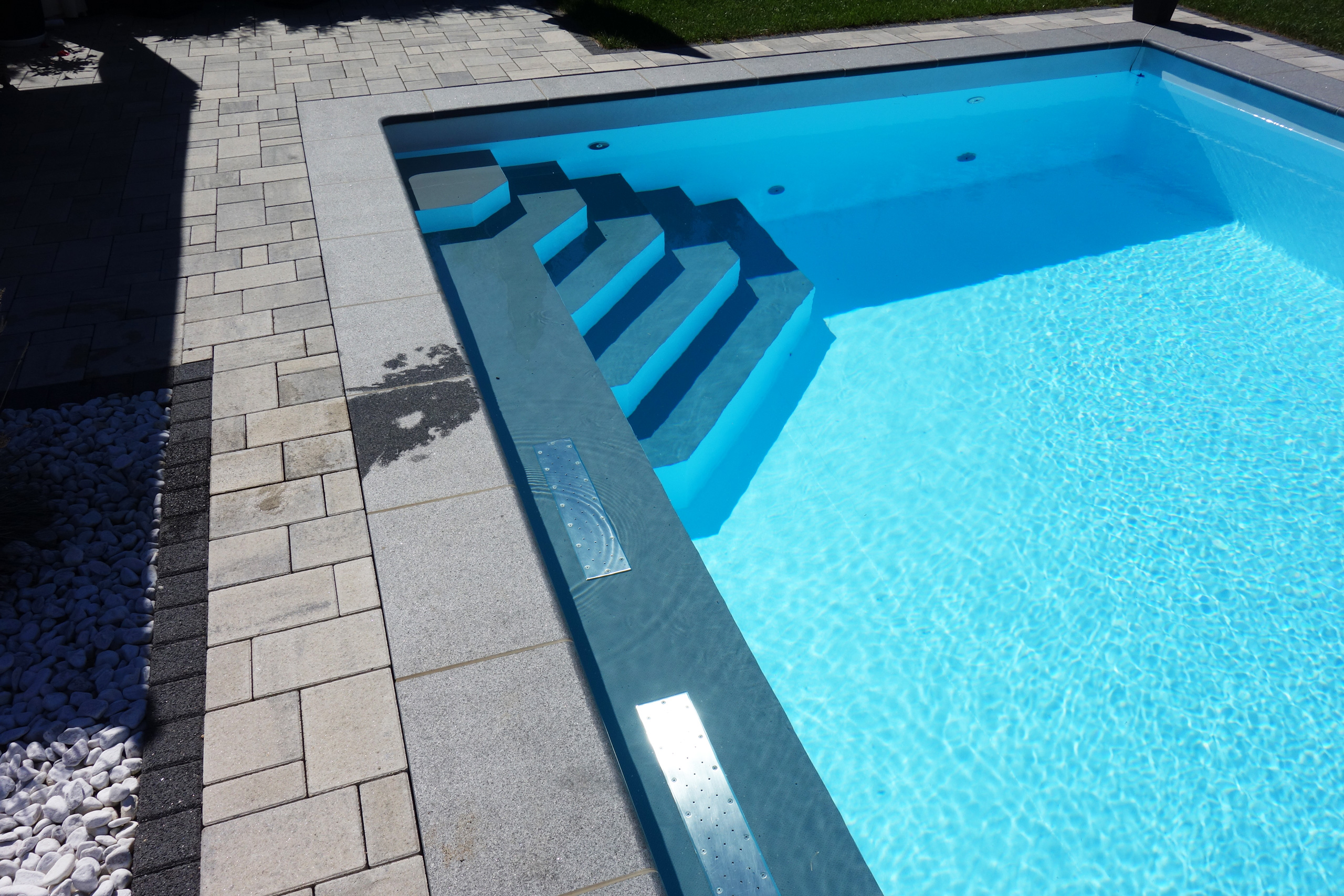Luftsprudelsitz und Treppe des Rechteckbeckens mit blauem Wasser und gepflastertem Randbereich