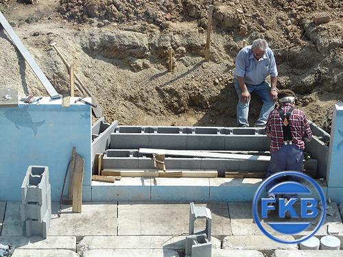 Zwei Männer bauen eine Treppe aus Betonsteinen für eine Beckensanierung in Hellblau.