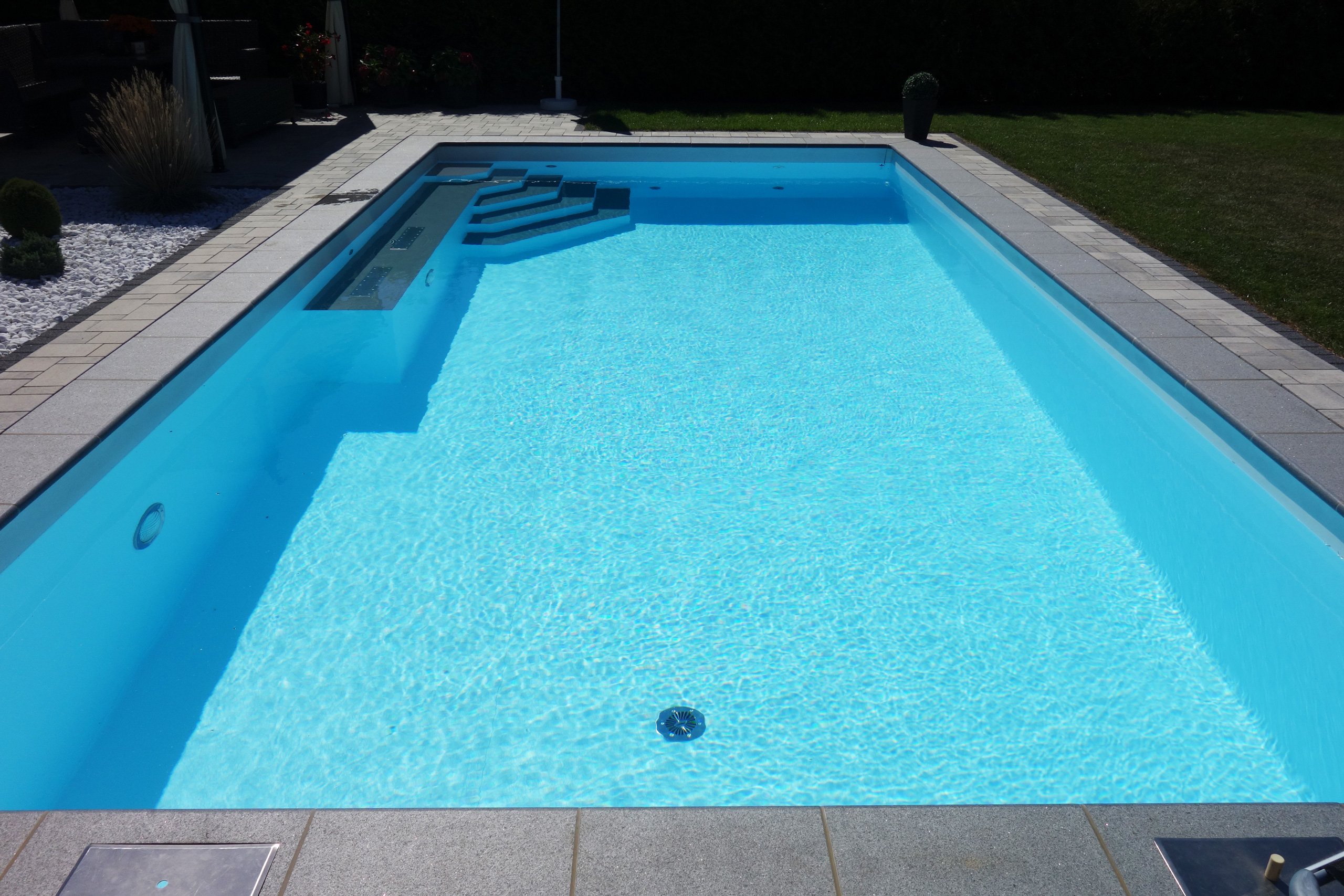 Rechteckbecken mit Ecktreppe, Podest und Luftsprudelsitz, umgeben von Pflastersteinen und Rasen