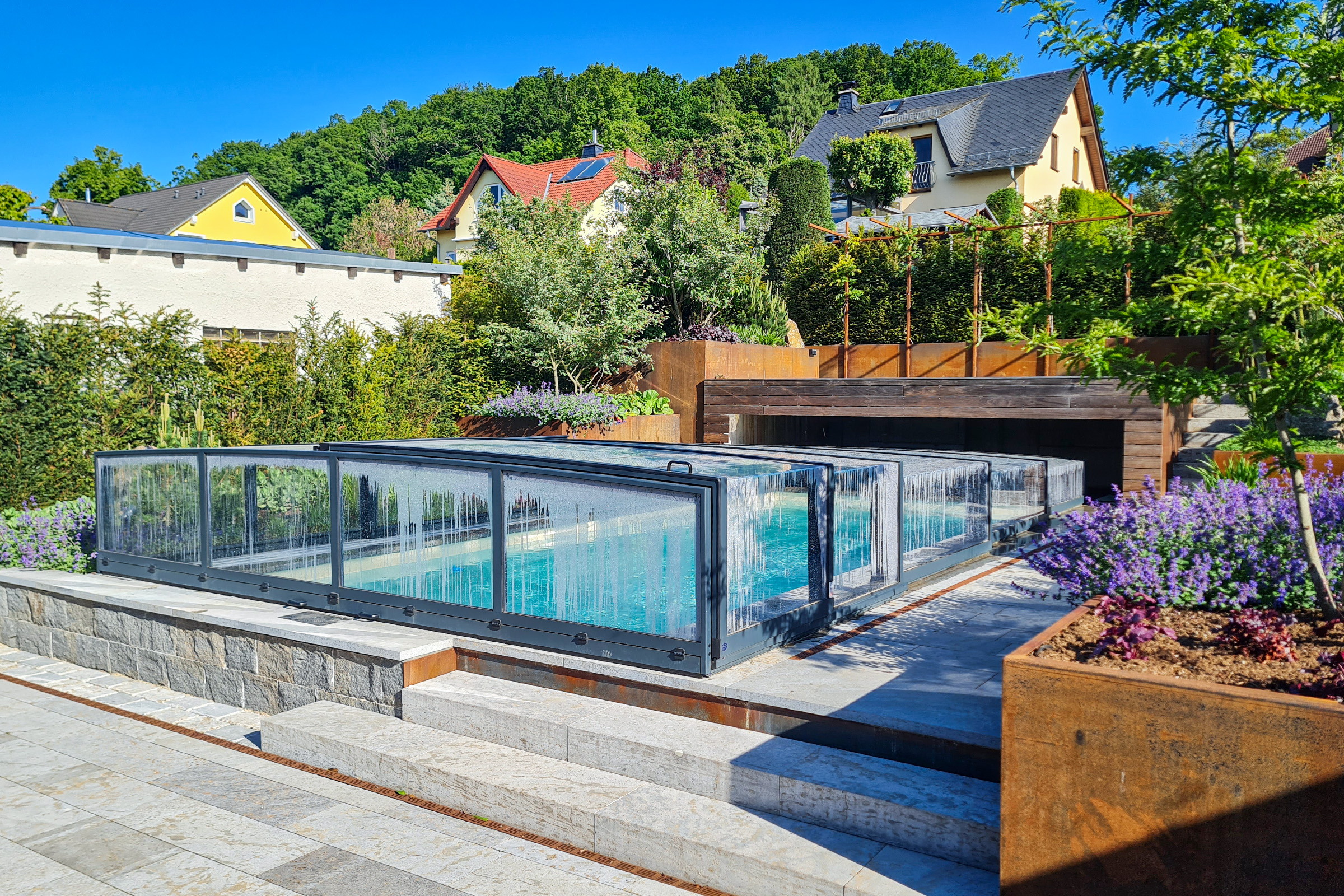 Flache Poolüberdachung auf Massivpool Pool mit Natursteinrand und farbenfrohem Garten
