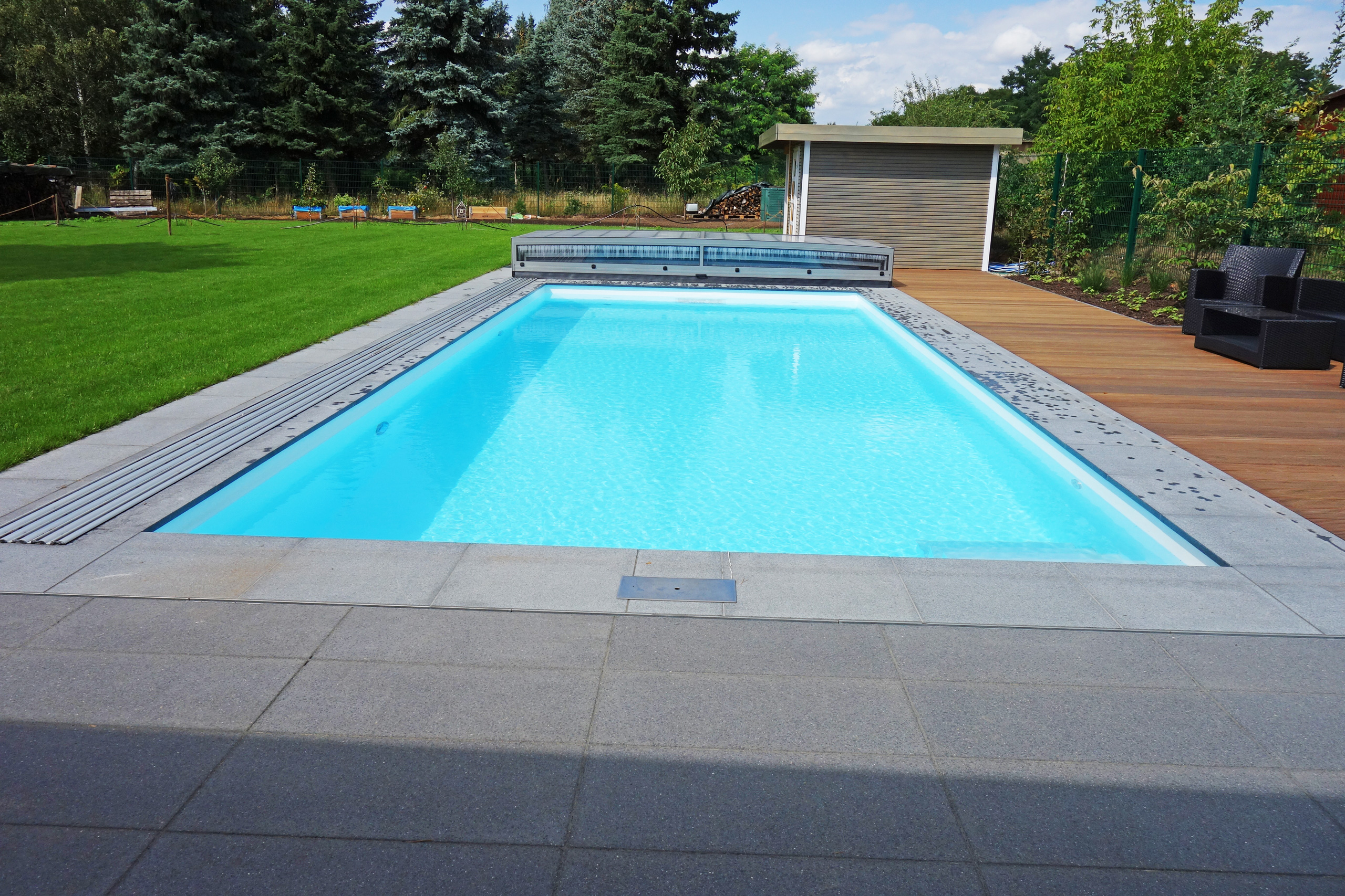 Rechteckiger Außenpool mit blauer Folie, grauen Fliesen und Holzterrasse, teilweise abgedeckt