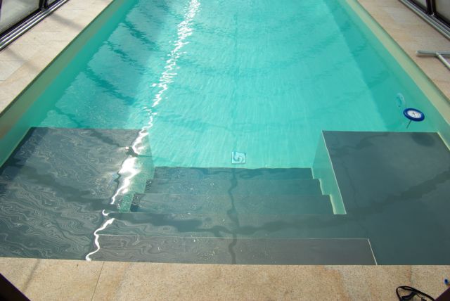 Innenliegende Treppe und Podest im Schwimmbecken, gefüllt mit türkisblauem Wasser