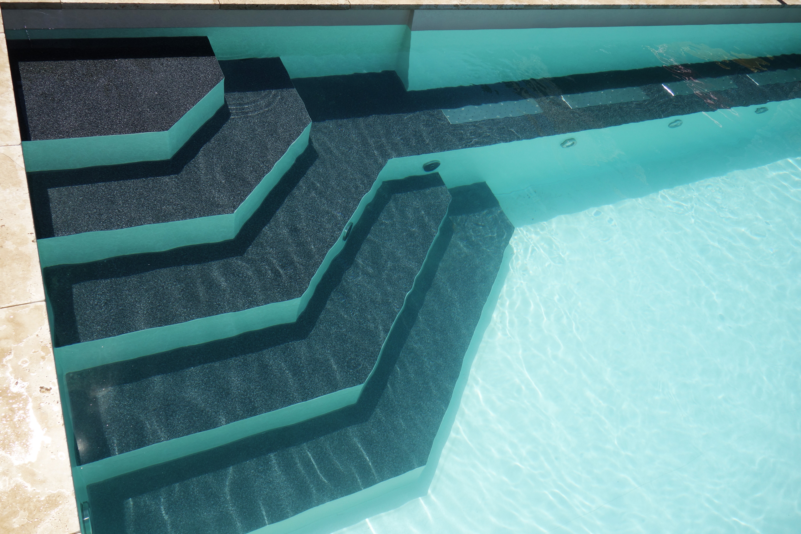 Dunkle Ecktreppe mit Sitzbank und Unterwasserbeleuchtung in einem Infinity Pool