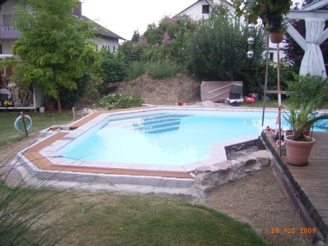 L-Form Schwimmbecken mit trapezförmiger Treppe, umgeben von Holz- und Steinumrandung im Garten