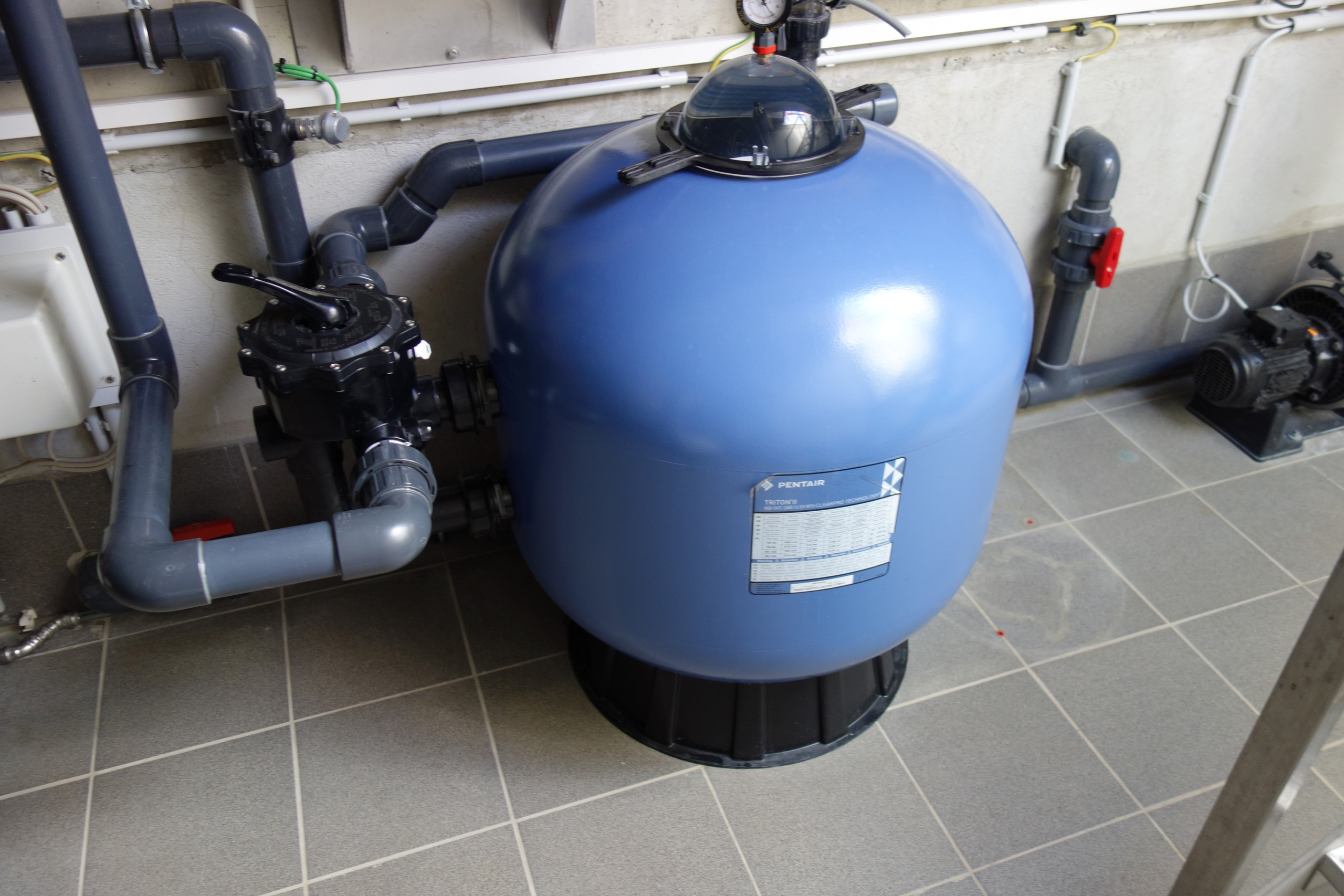 Detailansicht der Pooltechnik mit blauem Sandfilter und Verrohrung im Technikraum