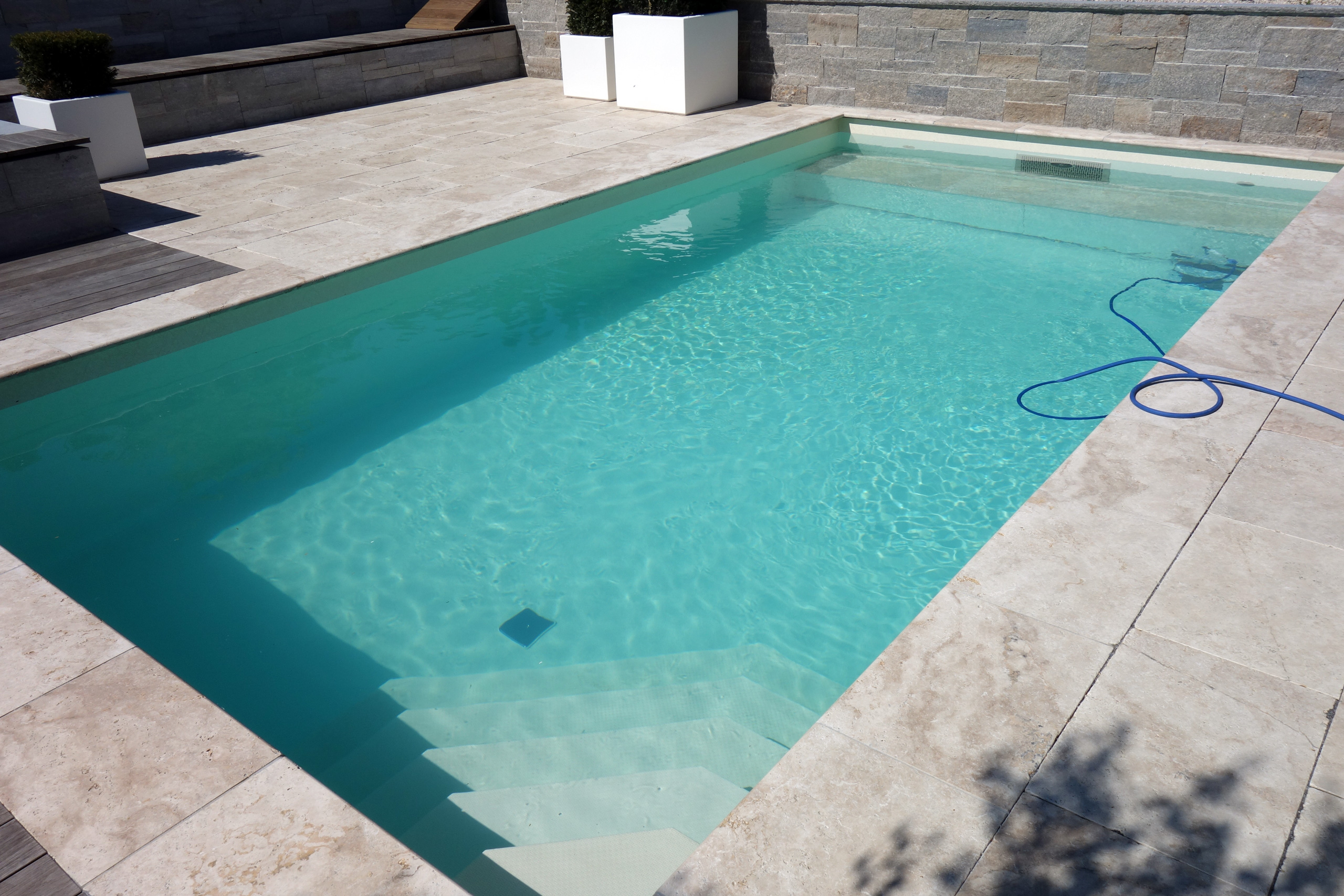 Schwimmbecken mit hellblauer Folie, breiter Treppe und einem blauen Schlauch am Beckenrand
